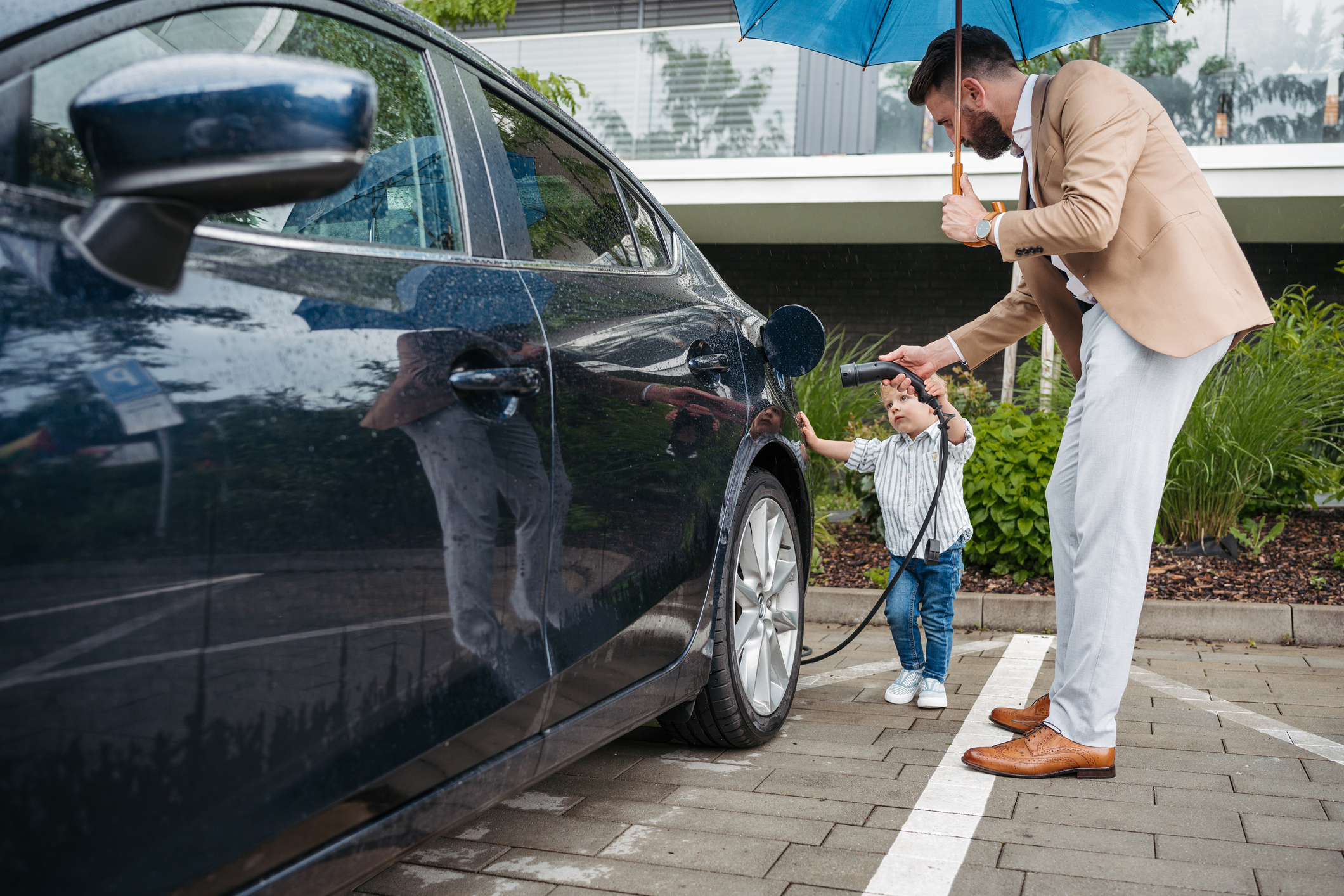 Toddler helping Dad plug in his electric car, megatrend.