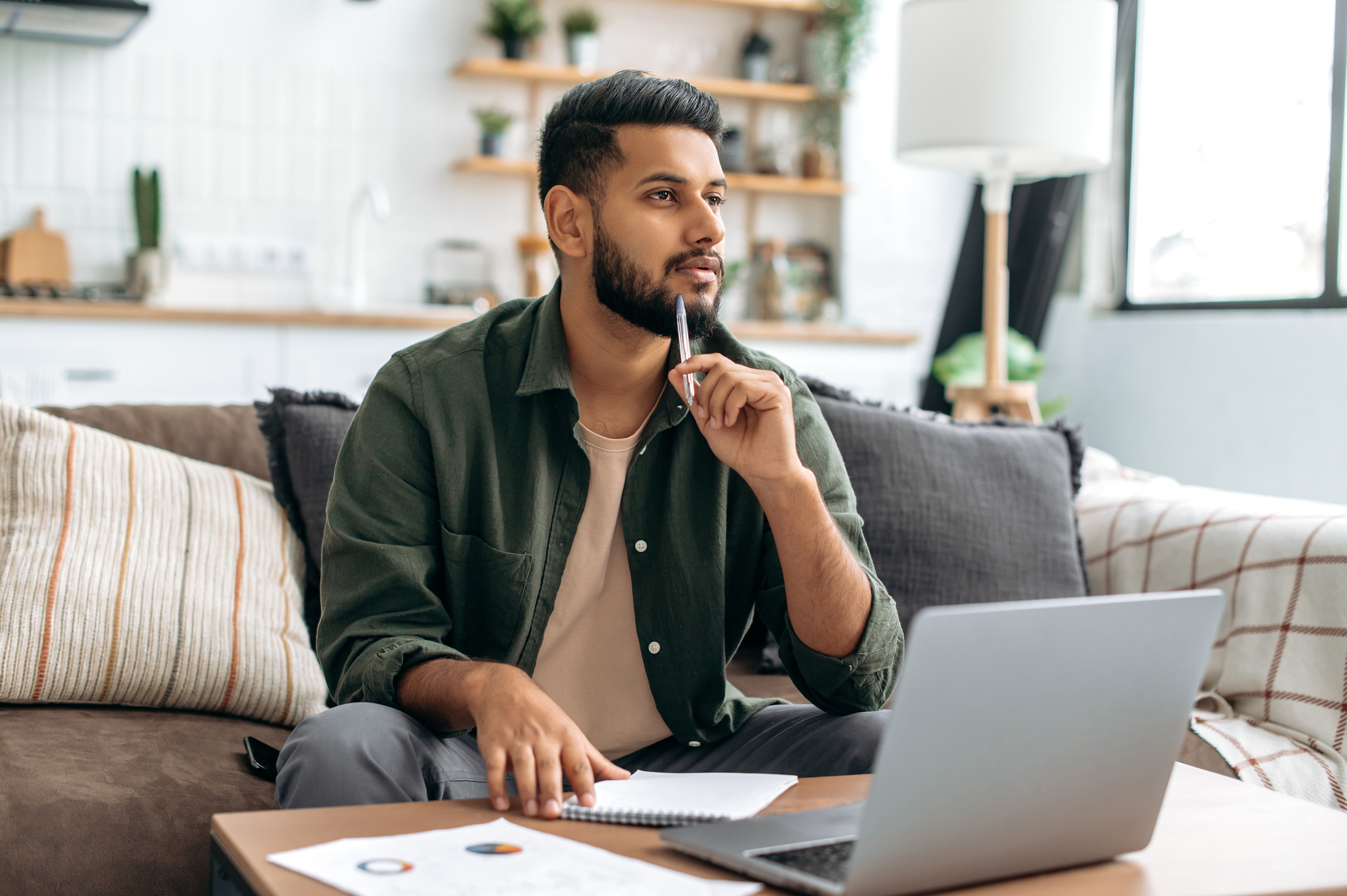 Young saver sitting on sofa with notepad, pen and laptop, checking out tax charges on savings