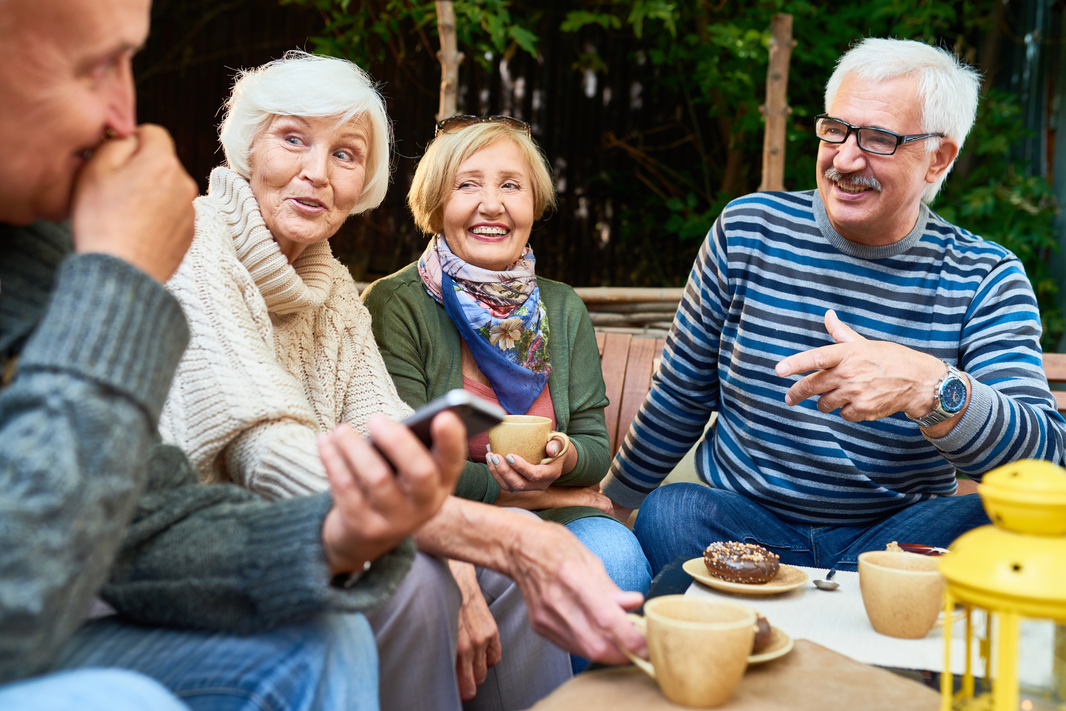 Group of pensioners sitting around a table drinking tea and coffee outside, early retirement