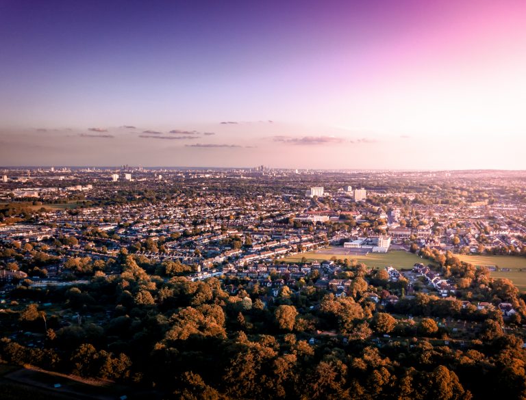 Fields and housing can be seen in the foreground and the City of London on the horizon, in Autumn light