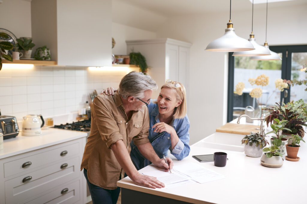 Middle age couple talking in the kitchen with tablet and pen and paper, talking about a mid life MOT